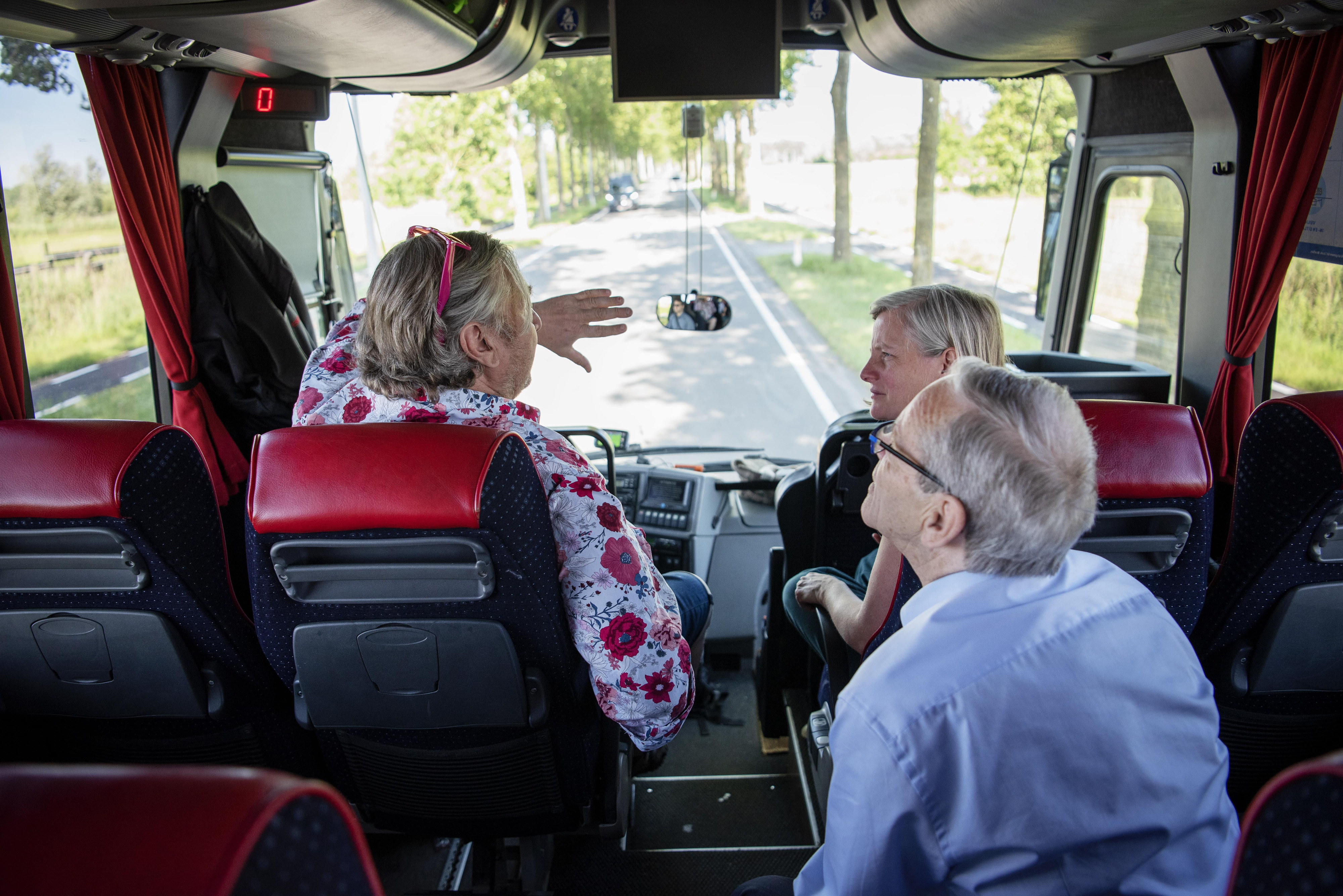 mensen die vooraan in de bus zitten en met elkaar praten, foto genomen van op de rug